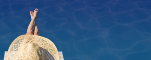 A woman wearing a hat sitting with legs in the pool.